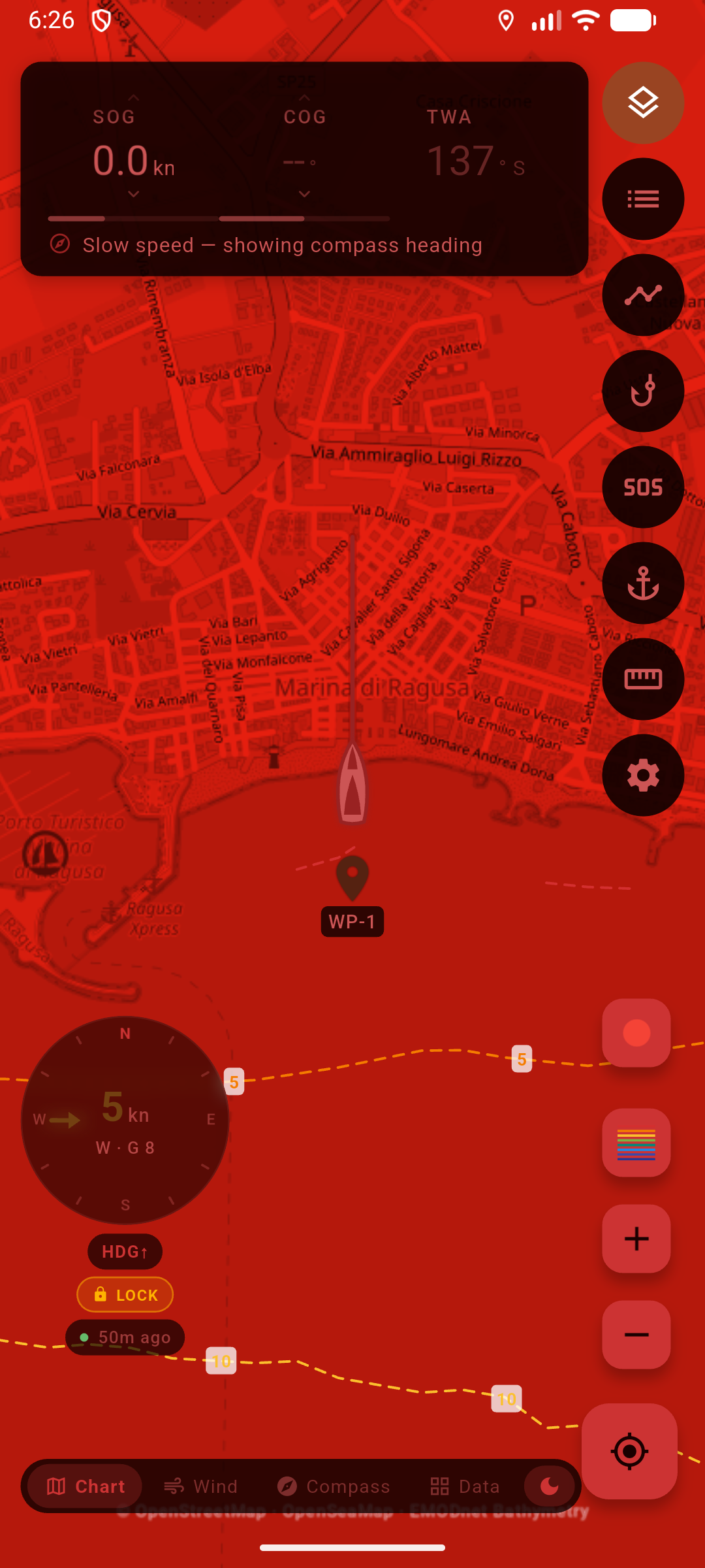 Chart helm in night vision: red-on-black map of Marina di Ragusa, moon chip on, Chart / Wind / Compass, SOS and instruments still readable.